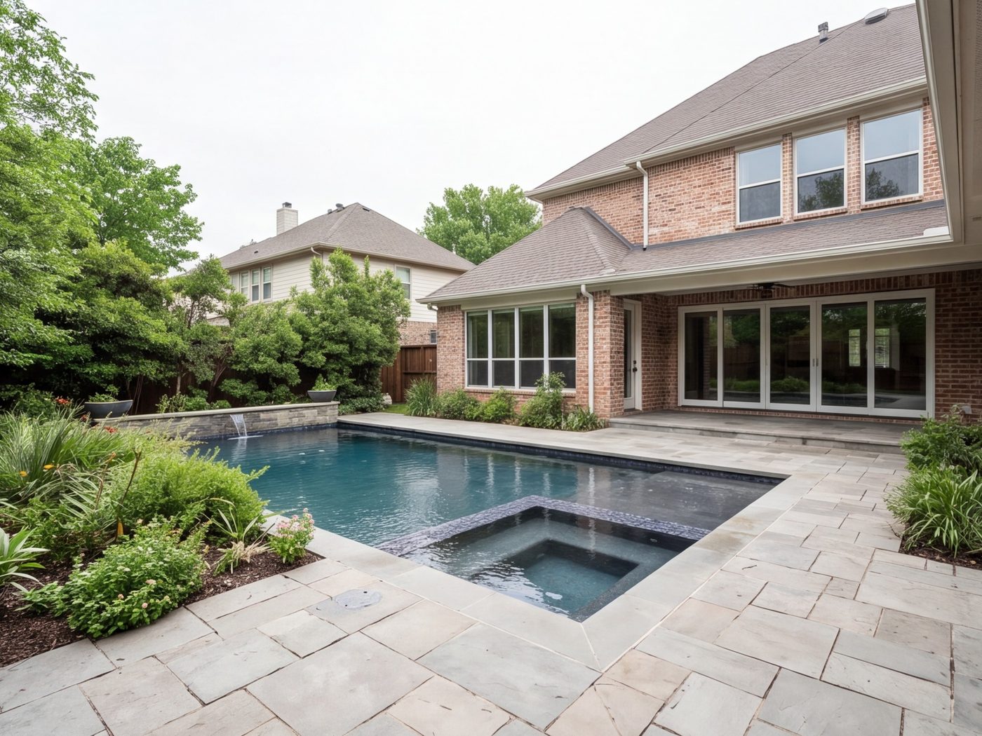 Back yard with a stone patio, pool deck and planting, house in frame