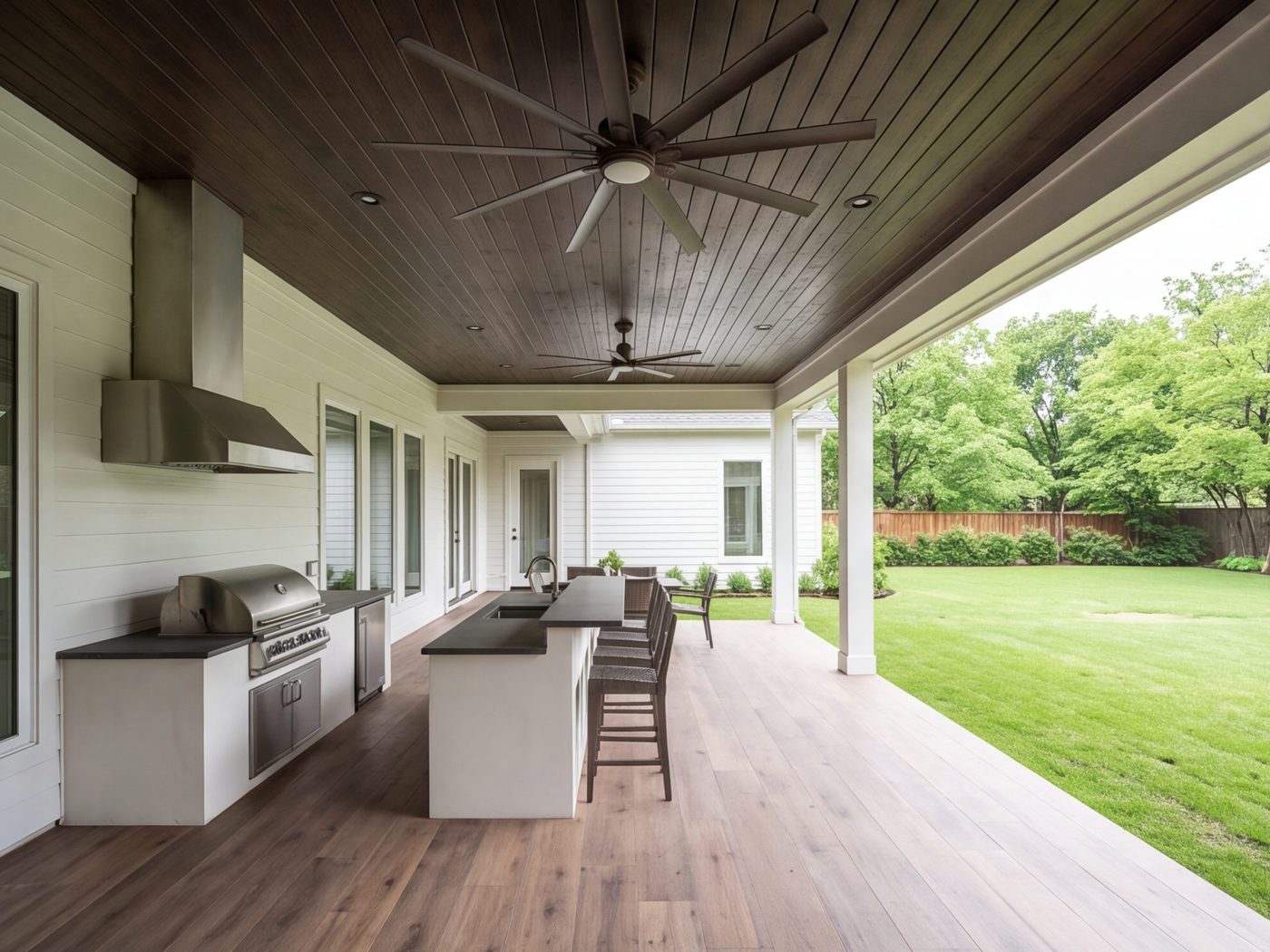 Covered patio with an outdoor kitchen, bar seating and ceiling fans, lawn beyond